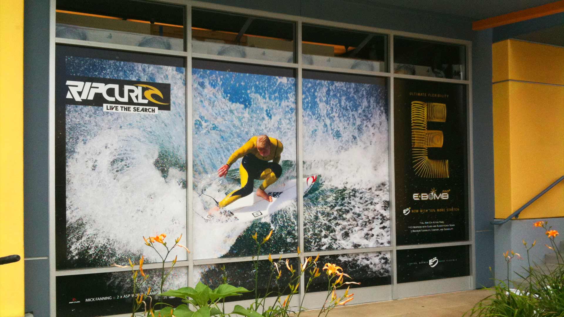 Perforated window of surfer in wetsuit on wave and black and gold Ebomb wetsuit logo